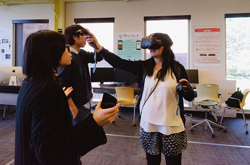Three students wearing and using virtual reality devices
