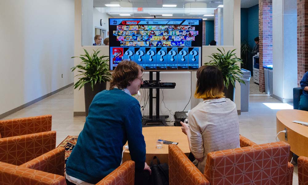 Two people in the Humanities Center are sitting and testing video games on a screen in front of them