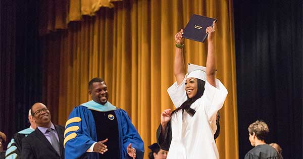woman holding up diploma during graduation ceremony