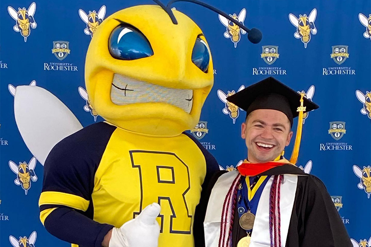 student in cap and gown posing with Rocky