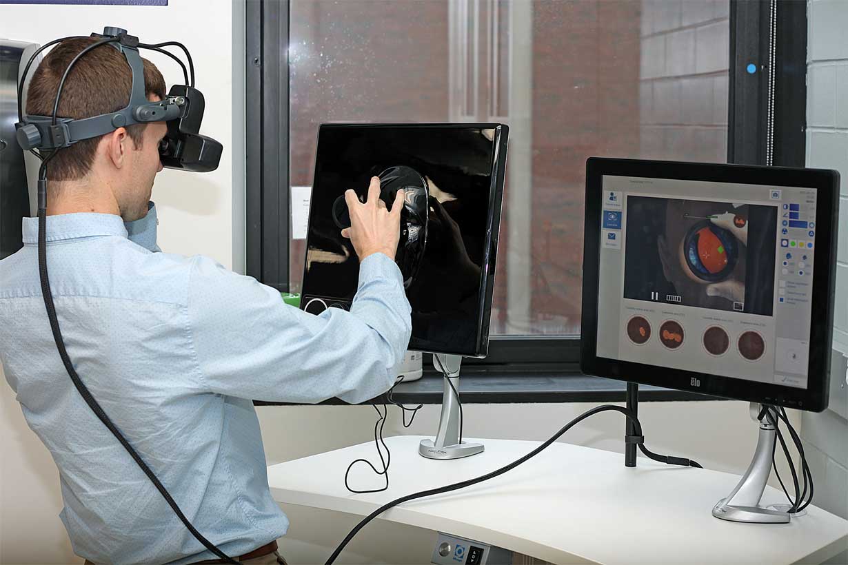 resident wearing headgear touches model of the human face next to a computer