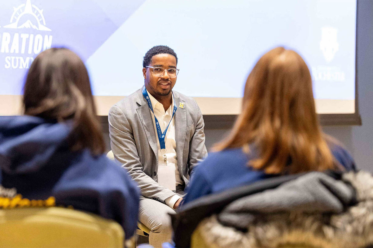 Jamal Holtz seated in front of two women in conversational setting