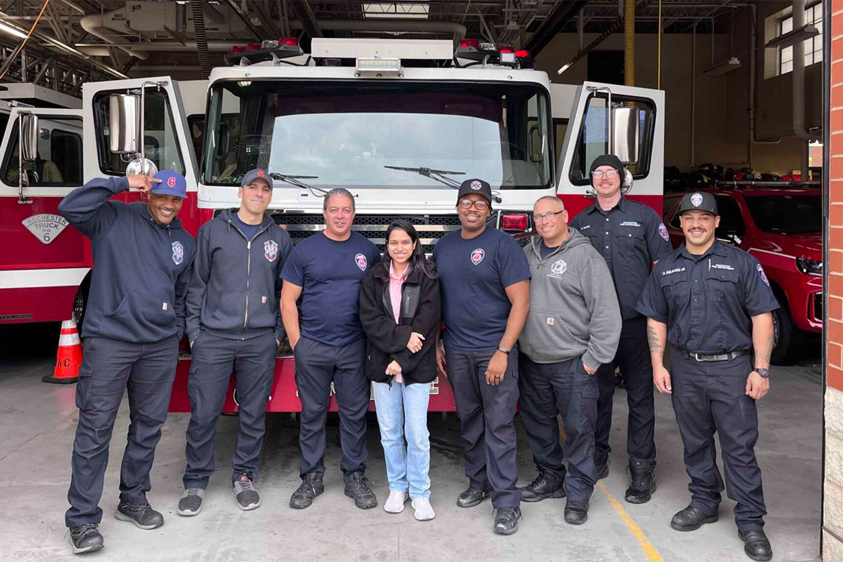 seven men and one women standing in front of fire truck at fire hall