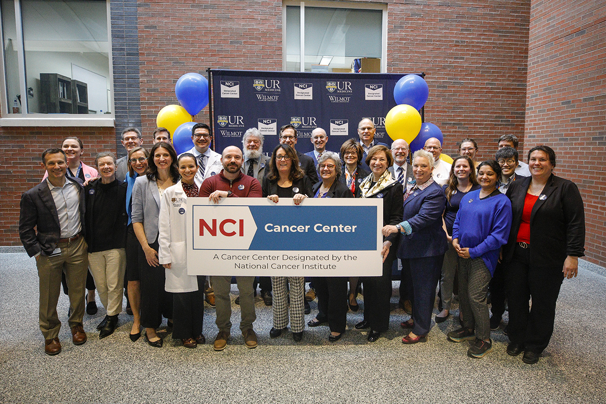 A group photo of ppl holding the NCI cancer center sign