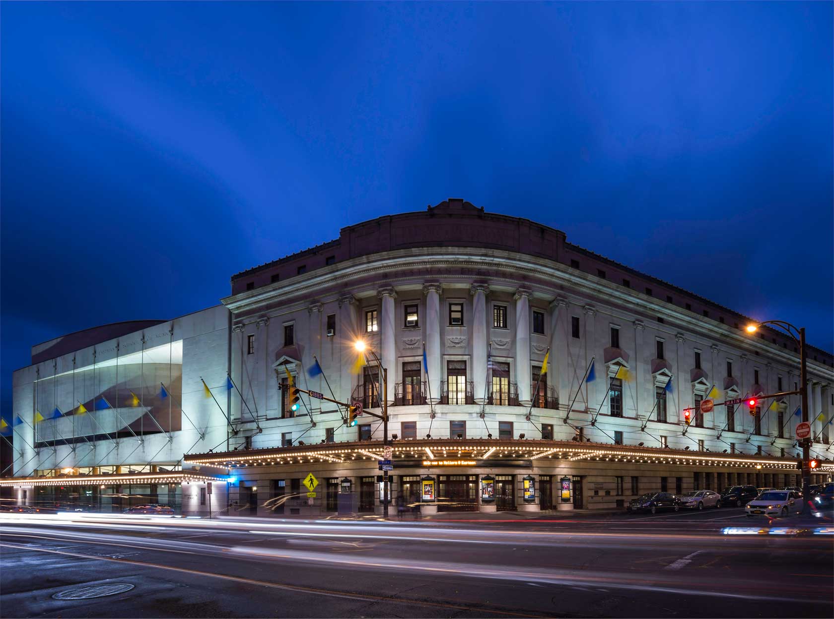 exterior view of the Eastman School of Music's Eastman Theater at dusk, with blue and yellow flags hung