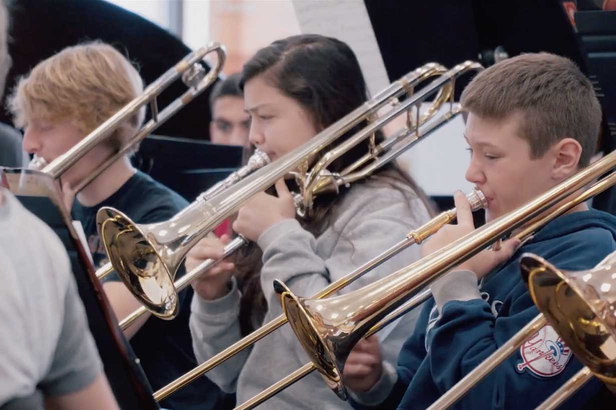 three students playing the trombone