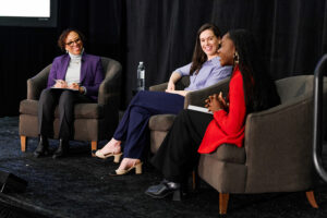 Three women sit on stage in armchairs during a panel discussion at the 2025 Women’s Summit, engaged in conversation about women’s leadership at the University.