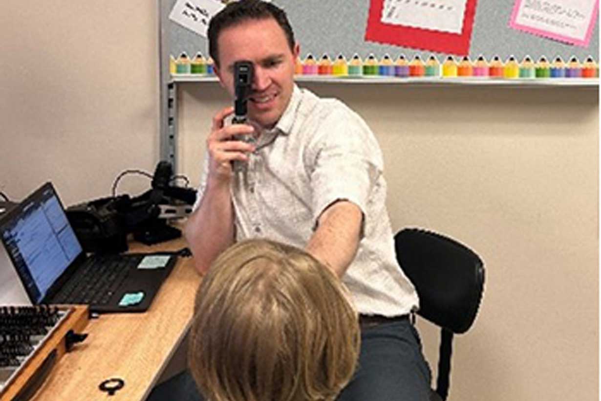 doctor holds instrument to his eye to look at child's eyes