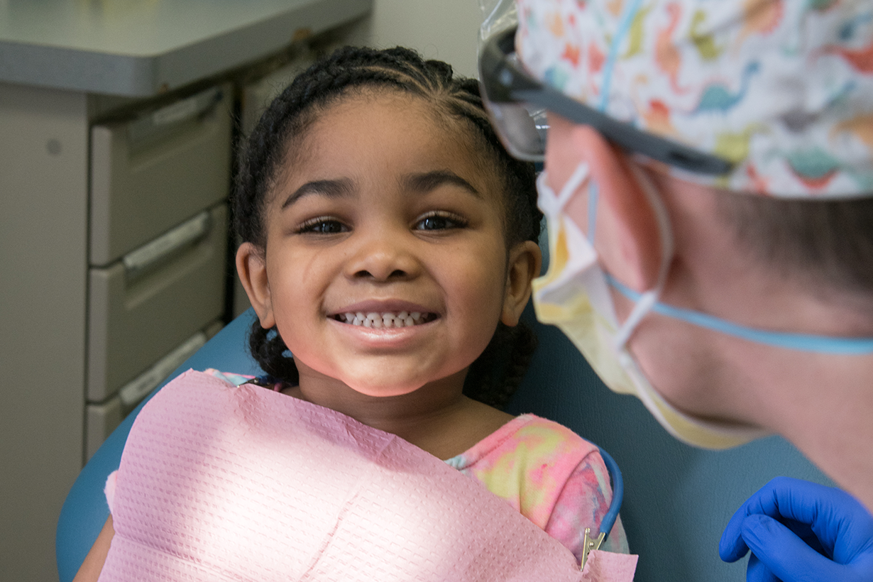 a young girl at the dentist smiling with a dental professional looking at her in the foreground