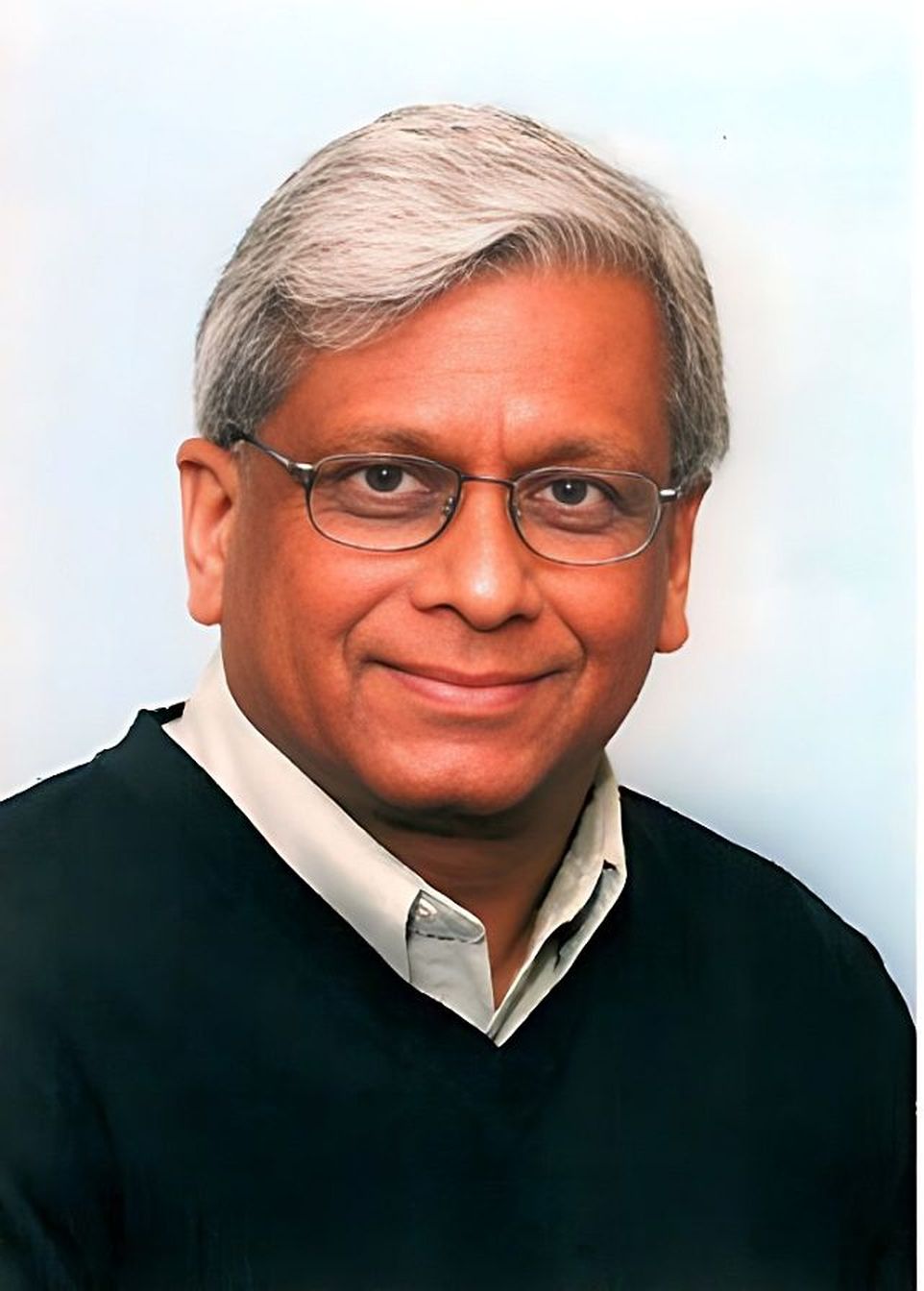 Govind P. Agrawal seen smiling, wearing glasses, a white collared shirt and a blue sweater