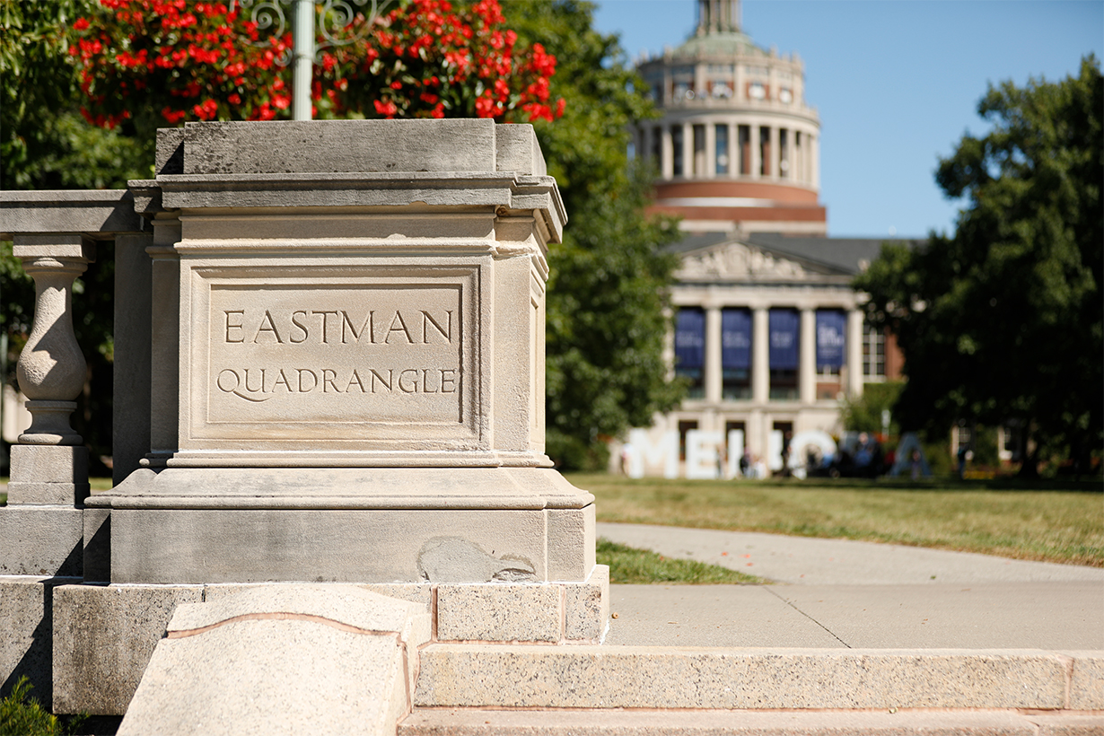 bannister column with "EASTMAN QUADRANGLE" carved into it with Rush Rhees library in the background