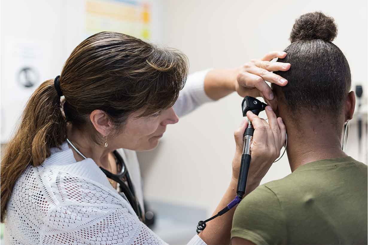 A nurse with a stethoscope checing a patient's ear