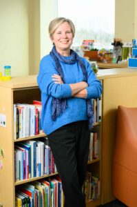 Lynn Cole, DNP ʼ98N (MS), ʼ21N posing with her arms folded, against a bookshelf