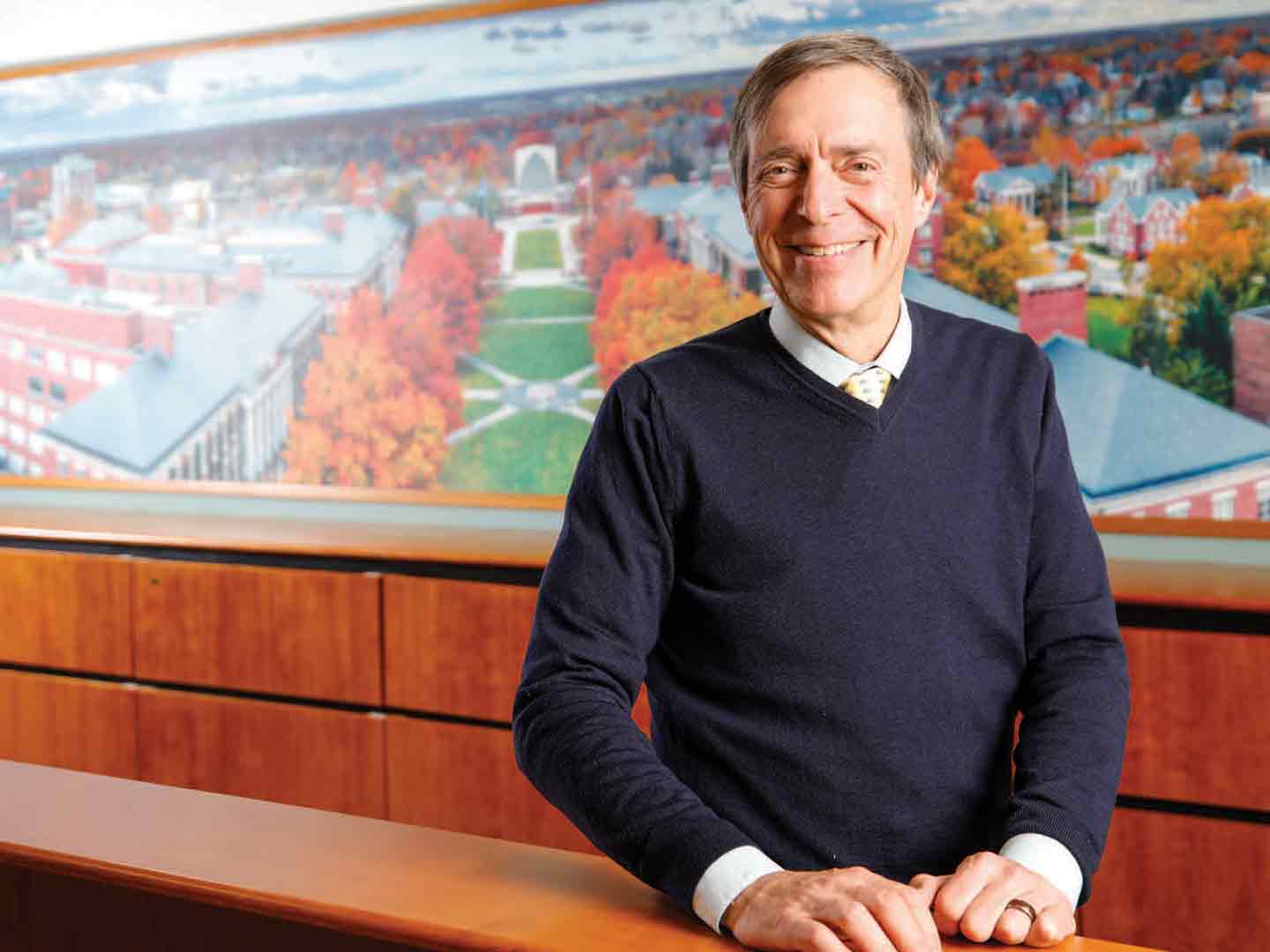 Doug Phillips smiling for camera, a wall is in the background that has a aerial image of river campus