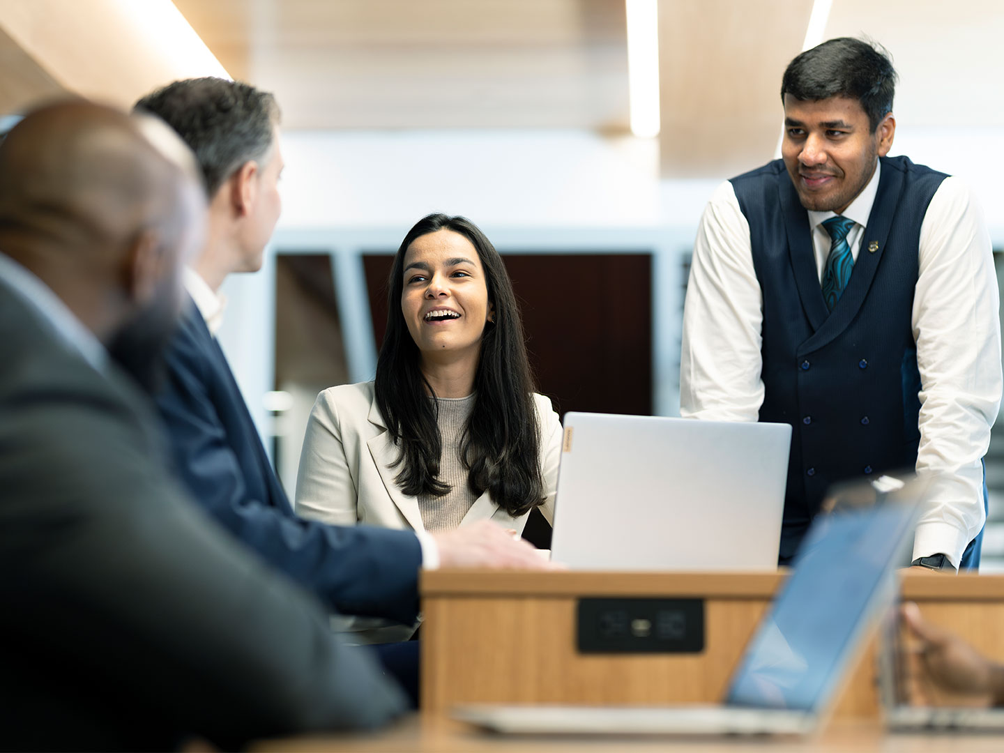 4 people in business attire around a desk with a laptop having a discussion